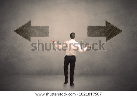 Business man taking a decision while standing in front of two grungy arrows on wall concept