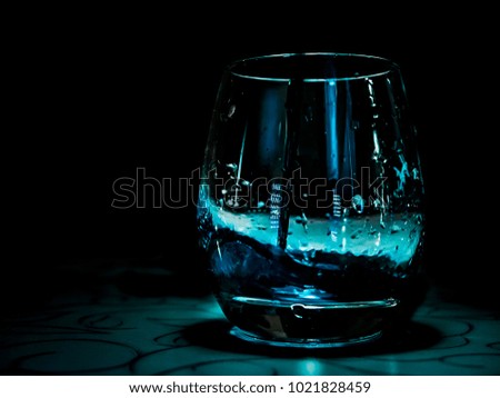 blue water drop into the glass on the table, black background