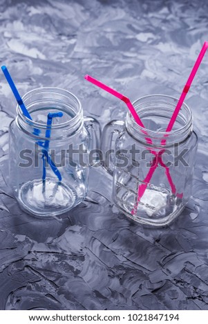 Empty drinking jars with colored drinking straws on a concrete table