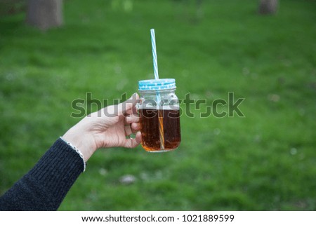 Woman's hand holding a cup of coffee and juice. beautiful outdoor green background. Drink, fashion, morning 