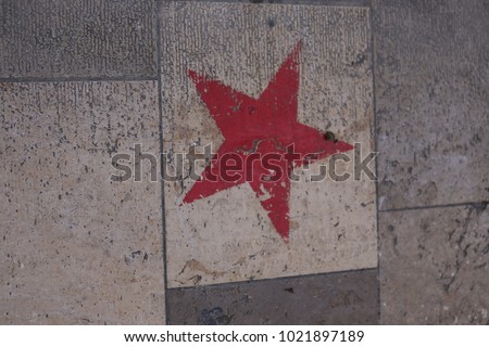 View of a red star painted on a paved street in a french city. Pattern composed with beige, yellow and grey stone rectangles. Isolated red element on a dirty surface. Abstract view, symbol of joy. 