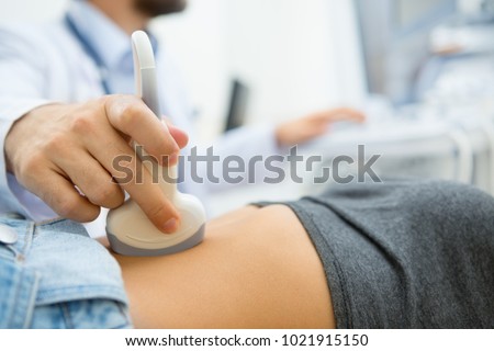 Selective focus on ultrasound scanner device in the hand of a professional doctor examining his patient doing abdominal ultrasound scanning sonogram sonography sonographer early pregnancy Royalty-Free Stock Photo #1021915150