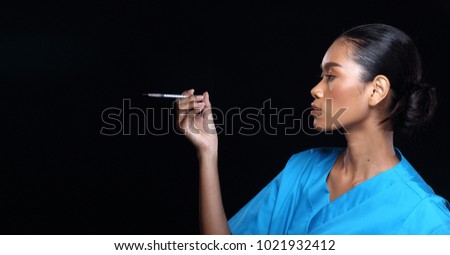 Asian Beautiful Doctor Nurse tan skin woman in blue uniform with syringe, portrait half body make up black hair, studio lighting dark background copy space presentation area