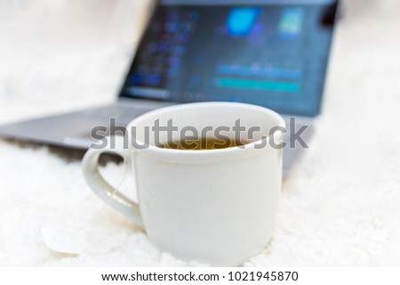 Hot tea in white mug in focus with laptop in background blurred out on white carpet remote work editing video