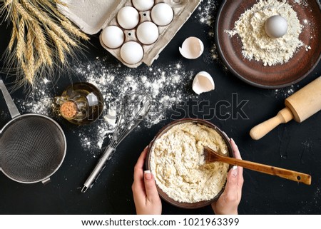 Female hands making/ mixing dough in brown bowl on black table, baking preparation close-up.