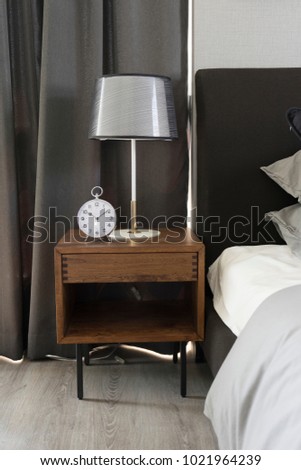 Modern Lamp With clock On Wooden Nightstand In Bedroom.
