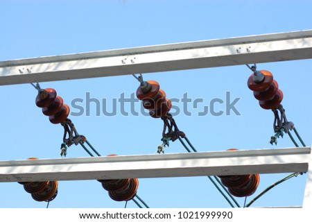 Rows of electrical wires with insulators mounted on bars at high voltage electrical substation against blue sky