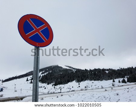 Blue-red warning sign on parking prohibition, dangerous road uphill in a Turkish ski resort in the winter afternoon in a snowstorm, Uludag, Turkey. 
