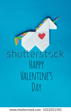 Handmade white trendy geometrical polygonal paper origami unicorn on blue background. Happy valentines day lettering, text, message. Vertical poster, postcard, banner, greeting card.