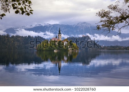 Autumn view of  the historical church on the island in Lake Bled before snow capped Alps with their reflection in water