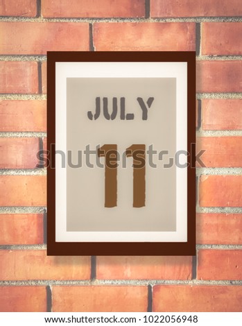 July 11th. 11 July calendar on the wood photo frame with brown brick background. Summer day