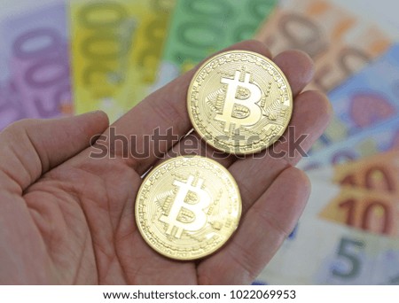 Hand with two big goden BITCOINS and blurred euro banknotes on the background