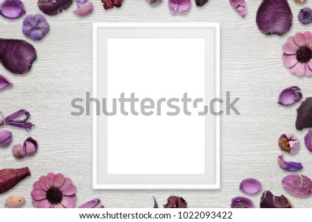 Picture frame with isolated white space for picture or text. Flower decorations around the frame. White wooden desk in background. Top view.
