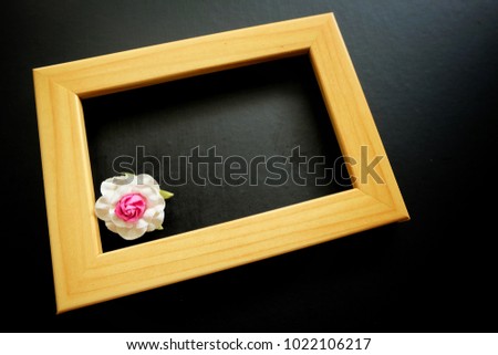 Paper flower and wooden frame on black background.