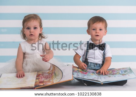 Cute kids in elegant clothes are looking at camera while playing with book, on light background