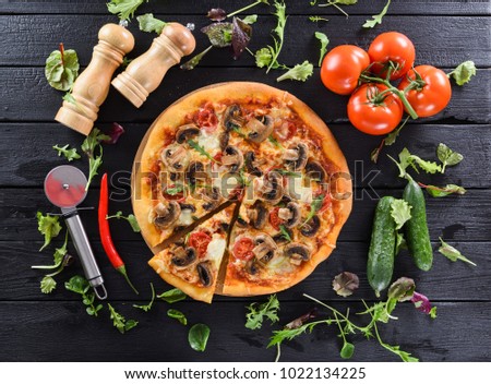 Healthy vegetarian pizza with mushrooms and tomatoes served with plenty of herbs and fresh vegetables on black background above view