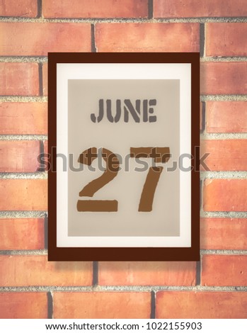 June 27th. 27 June calendar on the wood photo frame with brown brick background. Summer day