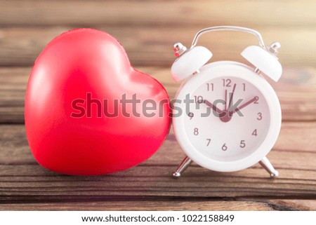 a red heart pattern, a white alarm clock on a wooden table background