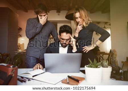 Three young coworkers working at modern studio on mobile laptop computer. Horizontal, blurred background.Visual effects