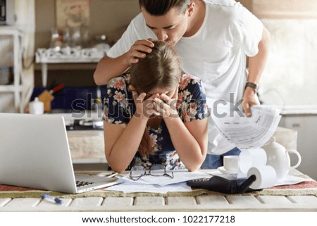 Sad woman covers face with hands, feels desperate and embarrased, recives bank invoice or bill, sit together with partnet at kitchen table, don`t see way out in difficult financial situation. Royalty-Free Stock Photo #1022177218
