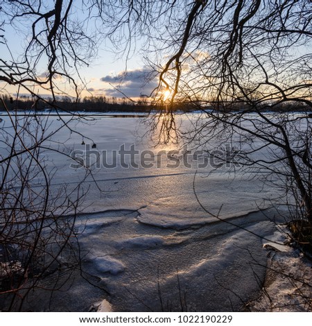 colorful winter sunset with light rays coming through the trees on the frozen river ice