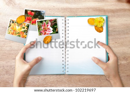 Hands holding note book with photo frame on wood background
