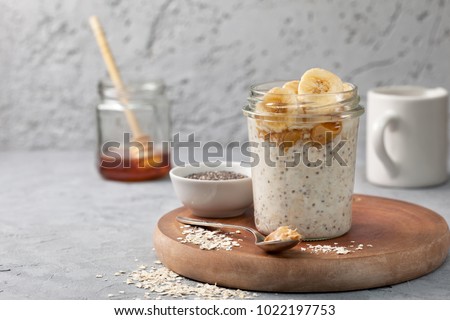 healthy diet breakfast. overnight oatmeal with chia seeds, bananas, peanut butter, honey in a glass jar on a gray concrete background Royalty-Free Stock Photo #1022197753