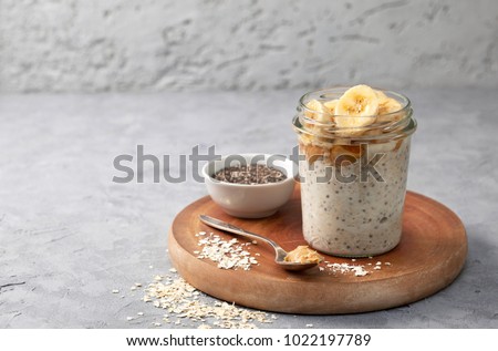 healthy diet breakfast. overnight oatmeal with chia seeds, bananas, peanut butter, honey in a glass jar on a gray concrete background Royalty-Free Stock Photo #1022197789