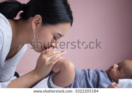 Portrait young mother kiss her baby child's foot. Mom nursing baby. mom and baby boy relax at home. Nursery interior. Mother breast feeding baby. Family at home. Mom's love.