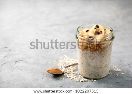 healthy diet breakfast. overnight oatmeal with chia seeds, bananas, peanut butter, honey, chocolate sprinkling in a glass jar on a gray concrete background Royalty-Free Stock Photo #1022207515