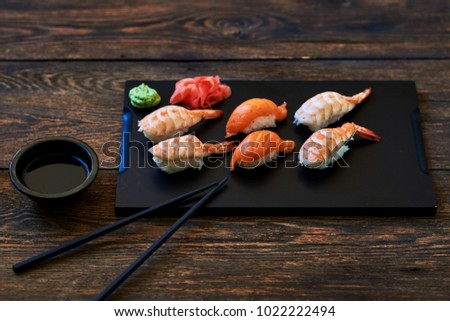 Food sushi background. Close up of sashimi sushi set with chopsticks and soy.  Japanese food restaurant,  sushi on dark background. Fresh made sushi set with salmon, prawns, wasabi and ginger.