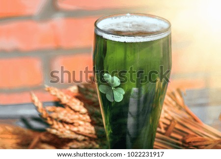 Green beer for St. Patrick's Day stands on an old wooden colored table along with beer ingredients - wheat, barley and snacks - nuts, pistachios, chips