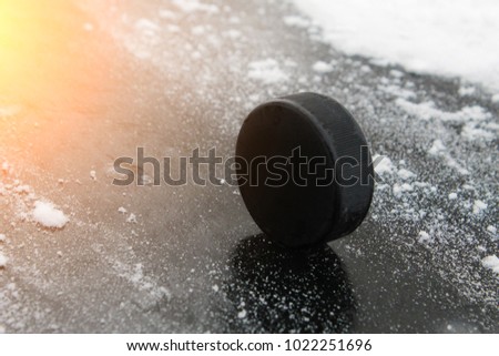 Black rubber hockey puck. With a place for text or images, isolated on snowy ice background. Fragment of ice hockey rink with. Color effect of the sun