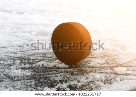 Black rubber hockey puck. With a place for text or images, isolated on snowy ice background. Fragment of ice hockey rink with. Color effect of the sun