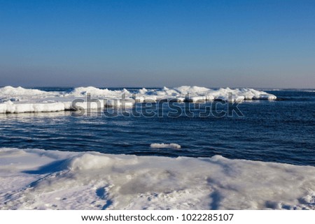 Sea coast in the cold season, around the snow and ice. Dark blue water, cloudless sky. Sunlight, far horizon line.