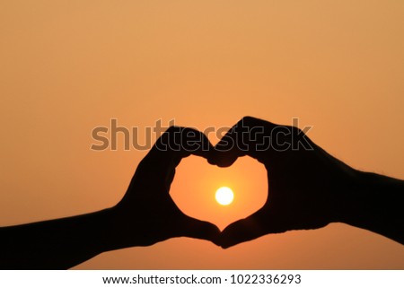 blurred silhouette a heart shape hand on sunset , mean love and relationship, hands in the form of heart against the sky pass sun beams