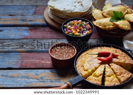 Mexican food mix - tacos, cornbread, salsa with tomato, red onion, lime, cilantro, corn and hot pepper sauce, empanadas. Copy space.
