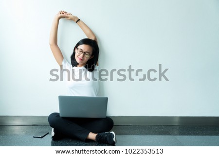 smiling beauty girl student sitting on floor with white wall background and looking at air daydreaming happy when she using laptop computer study.