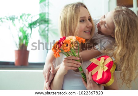 Little beautiful smiling girl hugging her mother and gives a gift in a box and a bouquet of flowers. Mothers Day. March 8. Women's Day.