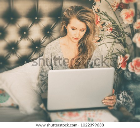 Beautiful woman in a gray pullover with flowing hair working on her laptop sitting on her bed at home