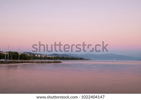 Scenic view of sunset over the Leman lake with pink sky with clouds and mountains in background in Switzerland