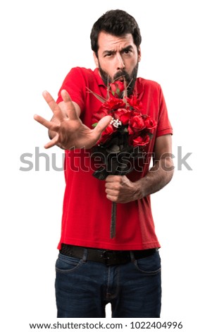 Handsome man holding flowers making stop sign over white background