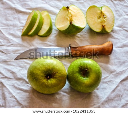 Green apples on a white tablecloth. Beautiful green large apples and a knife with a wooden handle. Finnish knife