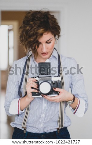 Beautiful girl with retro film medium-format camera looks into viewfinder and takes pictures. Film photographer.