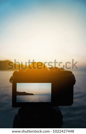 Camera setting at tripod to take photo or video of sunrise or sunset moment. selective focus at camera blurred sea in background. view of the sea in screen monitor. filtered image light effect added