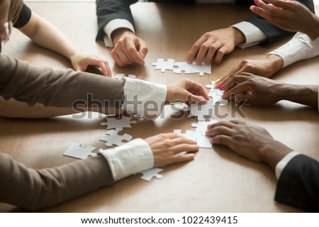 Diverse business people helping in assembling puzzle, cooperation in decision making, team support in solving problems and corporate group teamwork concept, close up view of hands connecting pieces Royalty-Free Stock Photo #1022439415