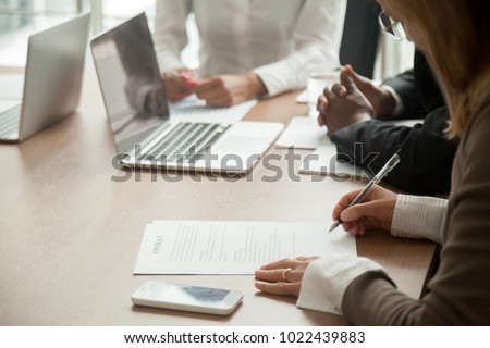 Businesswoman signing contract making legal deal with multiracial partners in bank, woman putting written signature on business document, taking commercial loan or insurance concept, close up view