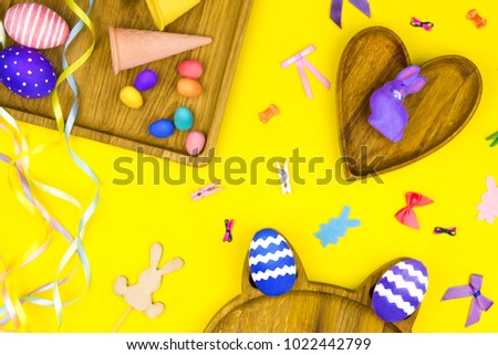 Happy Easter concept. Wooden plates in shape of heart, square and cat with colorful easter eggs, waffle cone and rabbit on yellow background with colorful bows and tapes