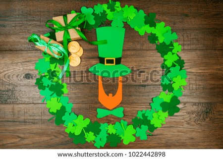 Saint Patrick's Day. Silhouette of leprechaun in hat lying on wooden background in circle shape of green three petal clovers, gift's box and gold coins