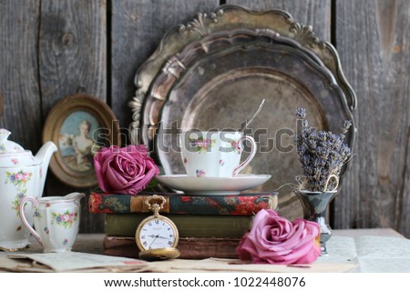 Composition with fresh roses, old books, porcelain coffee set, dread lavender in antique vase on round metal set silver ton plate background, gorgeous tea time and book reading image, vintage style